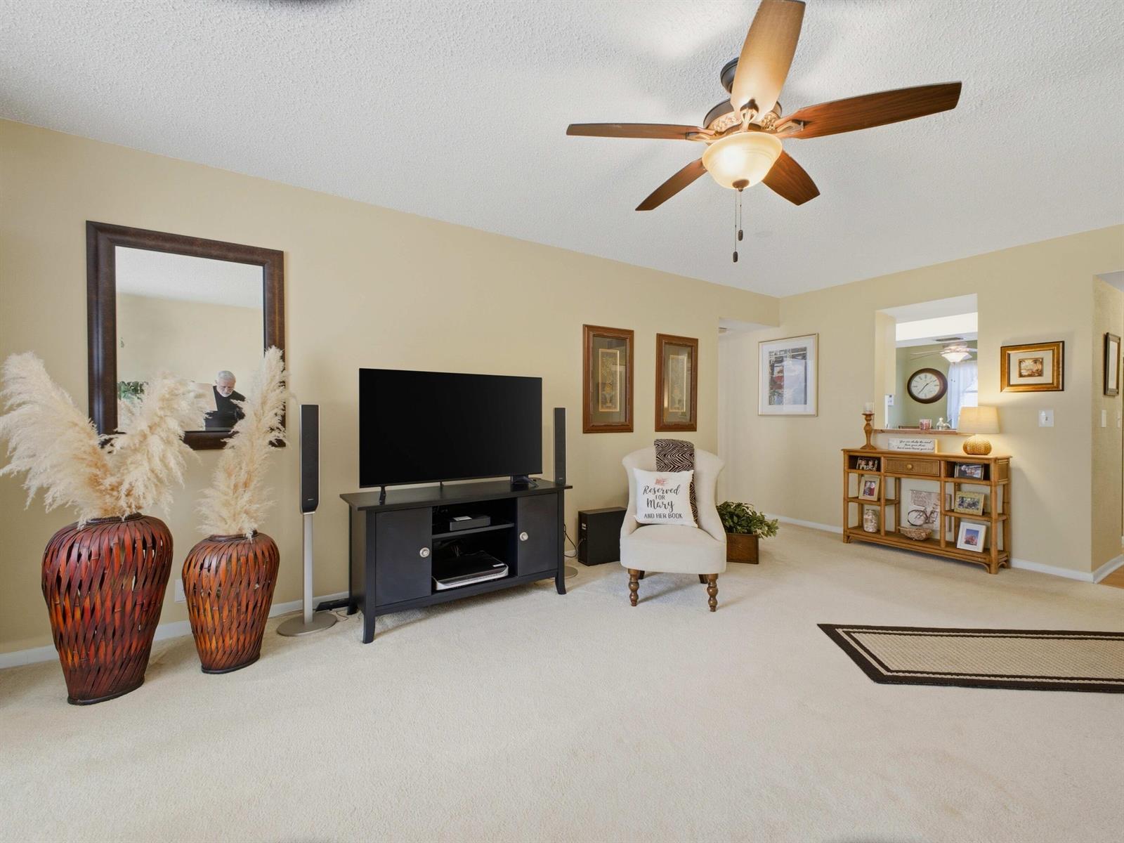 A living room features beige walls, carpeted flooring, a ceiling fan, and a television console — 6625 S Oriole Boulevard # 2040, Delray Beach FL 33446, DELRAY BEACH, FL