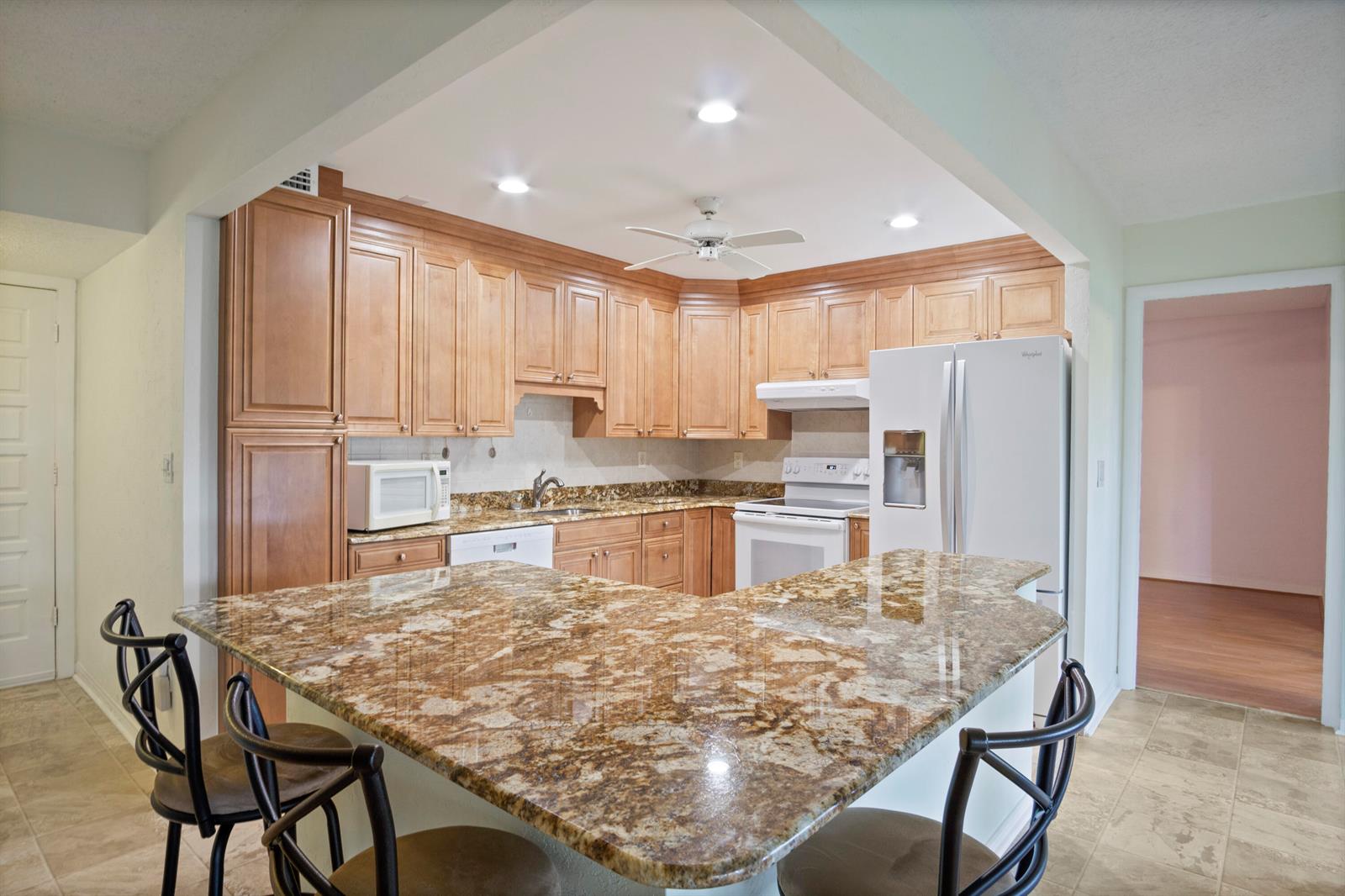 A kitchen features wood cabinets, granite countertops, a breakfast bar, and white appliances — 1800 SE Saint Lucie Boulevard # 204, Stuart FL 34996, STUART, FL