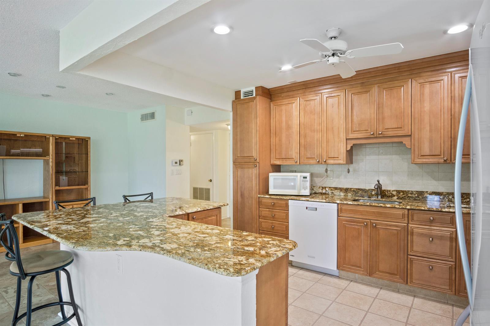 A kitchen features wood cabinets, granite countertops, a white dishwasher, and a breakfast bar — 1800 SE Saint Lucie Boulevard # 204, Stuart FL 34996, STUART, FL