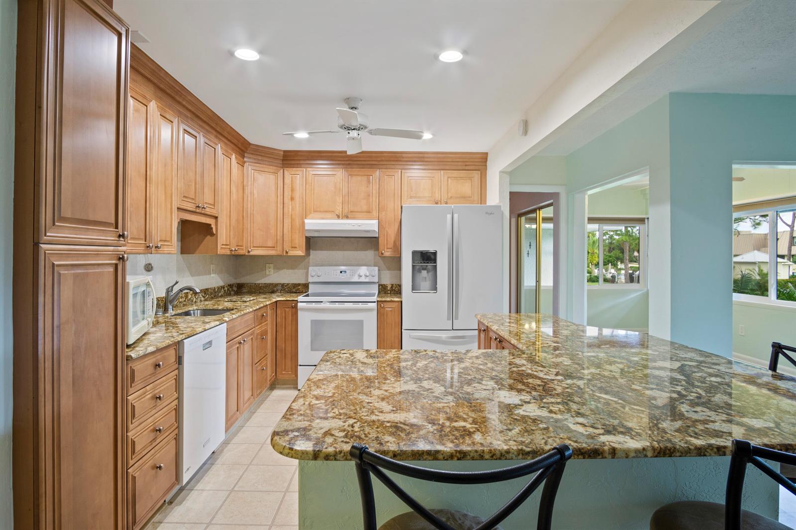 A kitchen features wood cabinets, granite countertops, white appliances, and a breakfast bar — 1800 SE Saint Lucie Boulevard # 204, Stuart FL 34996, STUART, FL