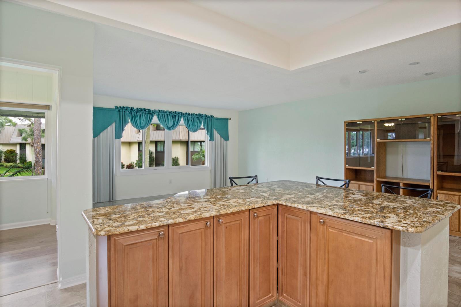 A kitchen island with granite countertops sits in front of a window with teal curtains — 1800 SE Saint Lucie Boulevard # 204, Stuart FL 34996, STUART, FL