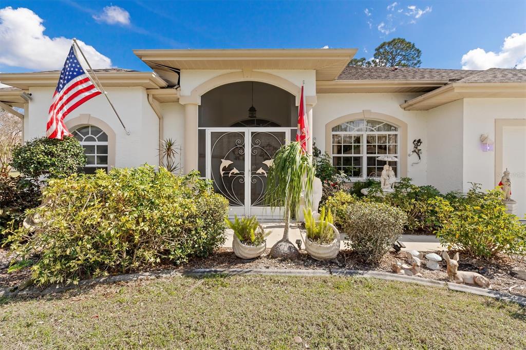 A single-story house exterior features a white stucco facade, a screened entryway, and an American flag — 3816 N CRANBERRY BOULEVARD, NORTH PORT, FL