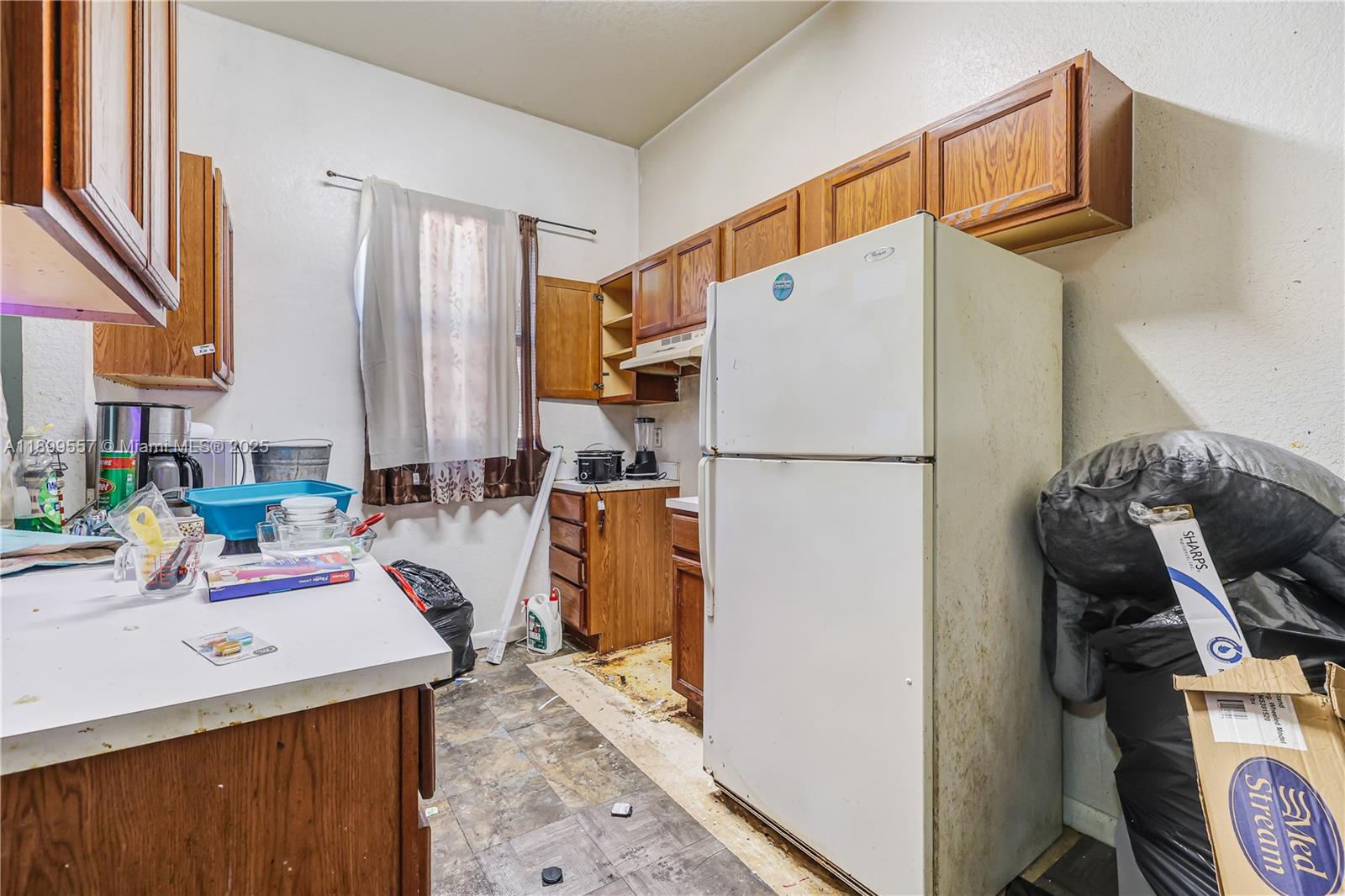 A kitchen features wood cabinets, a white refrigerator, and worn flooring with visible debris — 6960 NW 4th Ave # 3, Miami FL 33150, MIAMI, FL