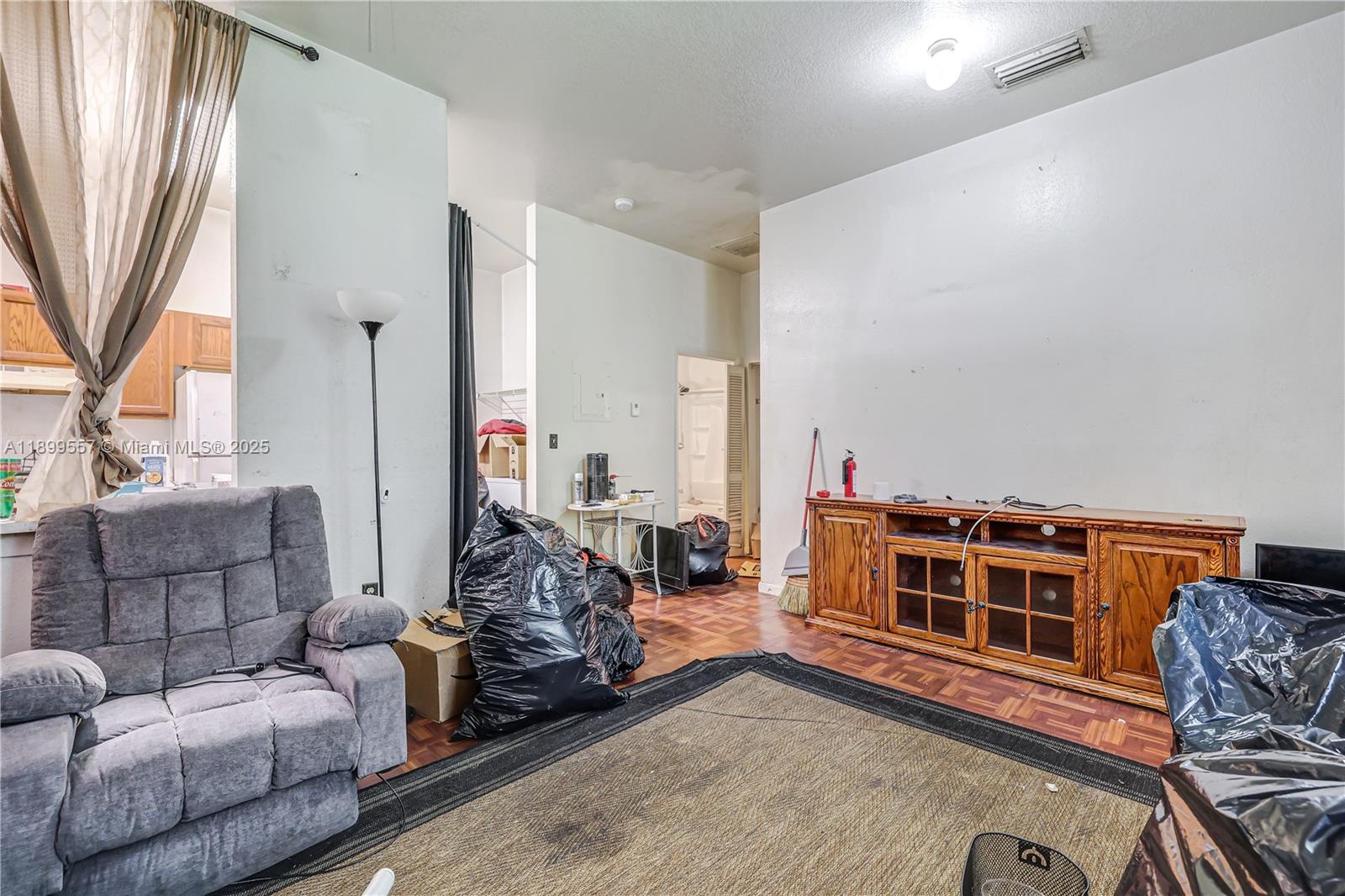 A living room features a gray recliner, a wooden media console, and parquet flooring — 6960 NW 4th Ave # 3, Miami FL 33150, MIAMI, FL