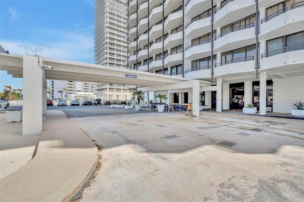 A concrete porte-cochère extends from a multi-story white building over a paved parking area — 2900 N ATLANTIC AVENUE NW UNIT 703, DAYTONA BEACH, FL
