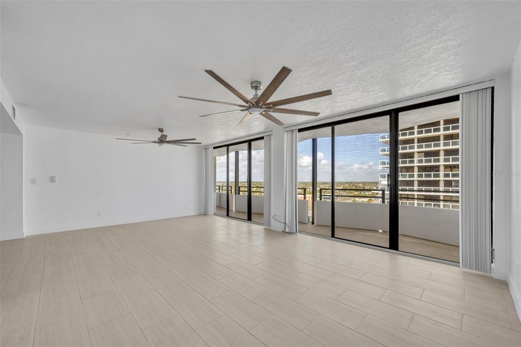 A bright, empty room features light-colored tile flooring, two ceiling fans, and large sliding glass doors — 2900 N ATLANTIC AVENUE NW UNIT 703, DAYTONA BEACH, FL