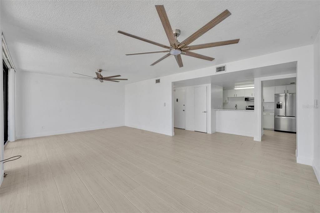 An open-concept living area features light-colored tile flooring, two ceiling fans, and a kitchen — 2900 N ATLANTIC AVENUE NW UNIT 703, DAYTONA BEACH, FL