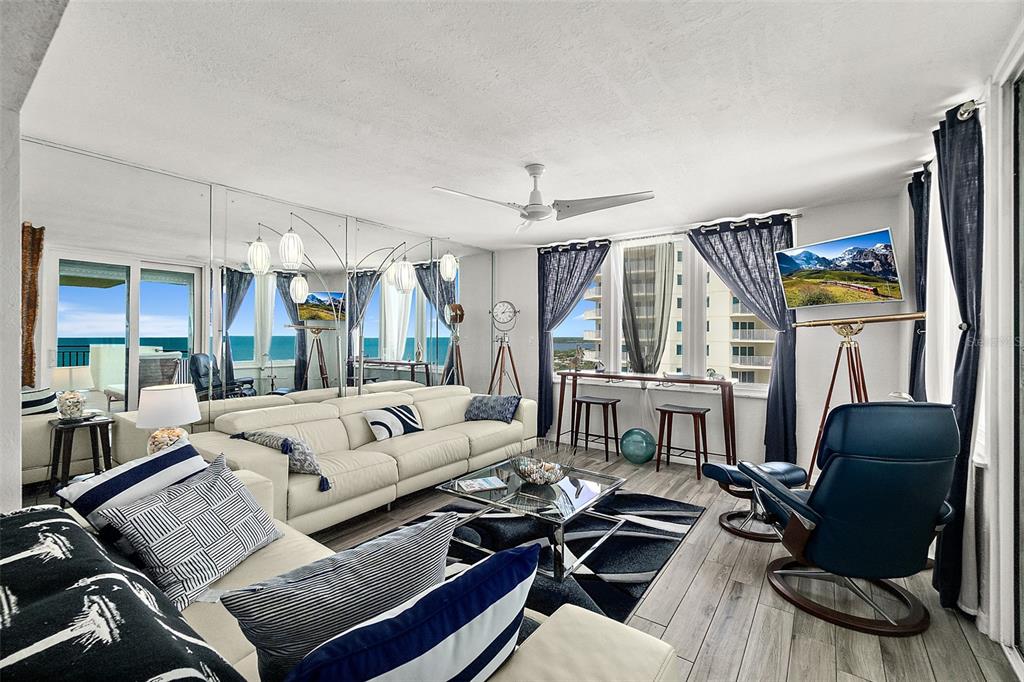 A living room with a white sectional sofa, mirrored wall, and ocean view through windows — 2947 S ATLANTIC AVENUE UNIT 1604, DAYTONA BEACH, FL