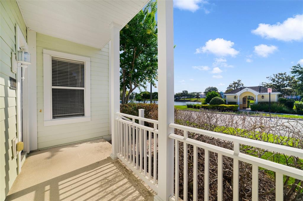 A covered porch with white railings overlooks a neighborhood street, a small lake, and landscaping — 7740 LINKSIDE LOOP UNIT 7740, KISSIMMEE, FL