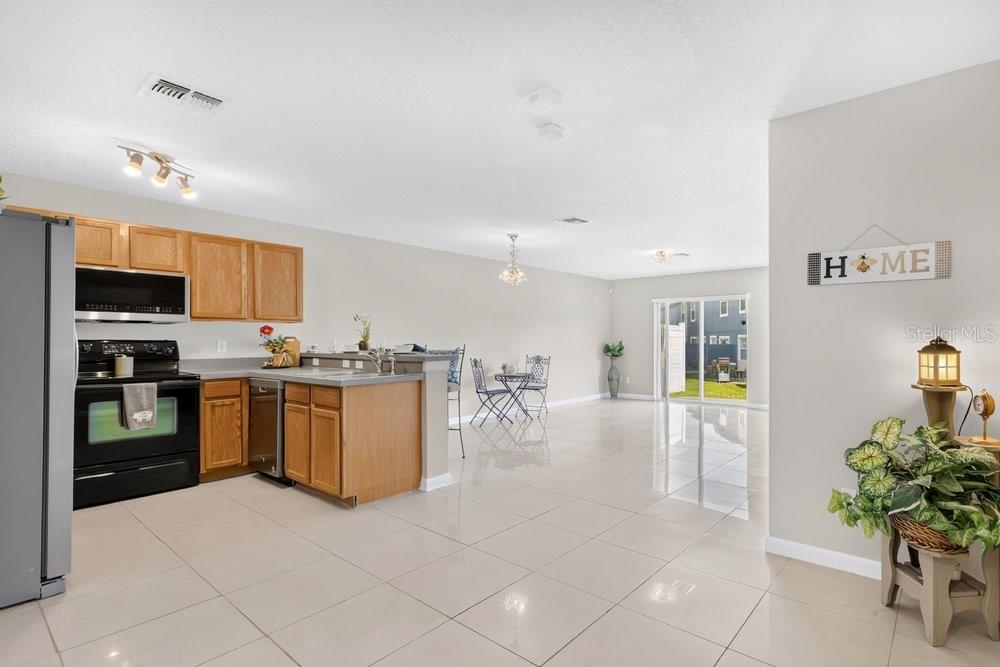 A kitchen with wooden cabinets and tile flooring opens into a bright, spacious living area — 12640 SOMERSET OAKS STREET, ORLANDO, FL