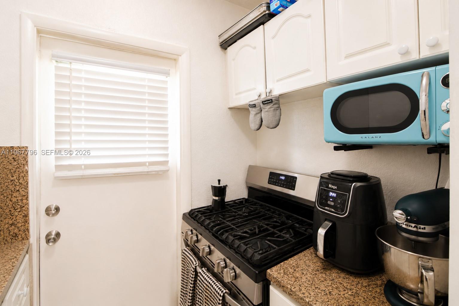 A narrow galley kitchen features white cabinets, granite countertops, a stainless sink, and white appliances — 3901 SW 78th Ct # 116, Miami FL 33155, MIAMI, FL