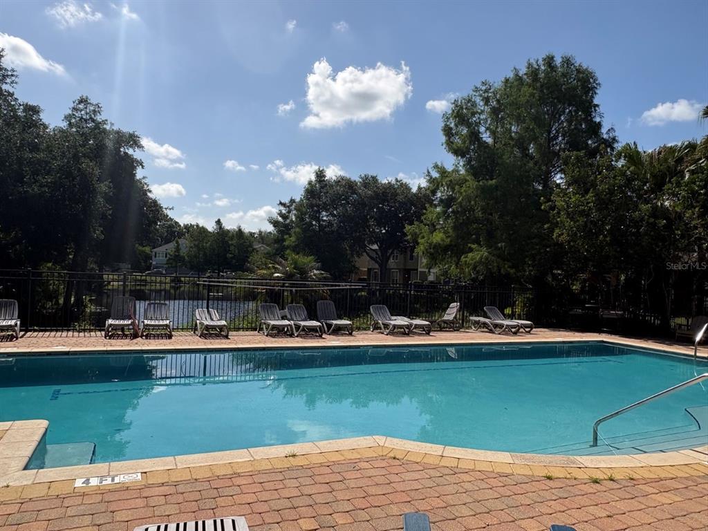 A swimming pool with lounge chairs on a brick deck overlooking a pond and trees — 1931 SAN JACINTO CIRCLE UNIT 1931, SANFORD, FL