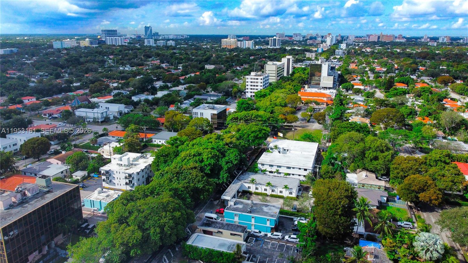 An aerial view shows a neighborhood with low-rise buildings, dense trees, and a distant skyline — 1875 SW 22nd St, Miami FL 33145, MIAMI, FL