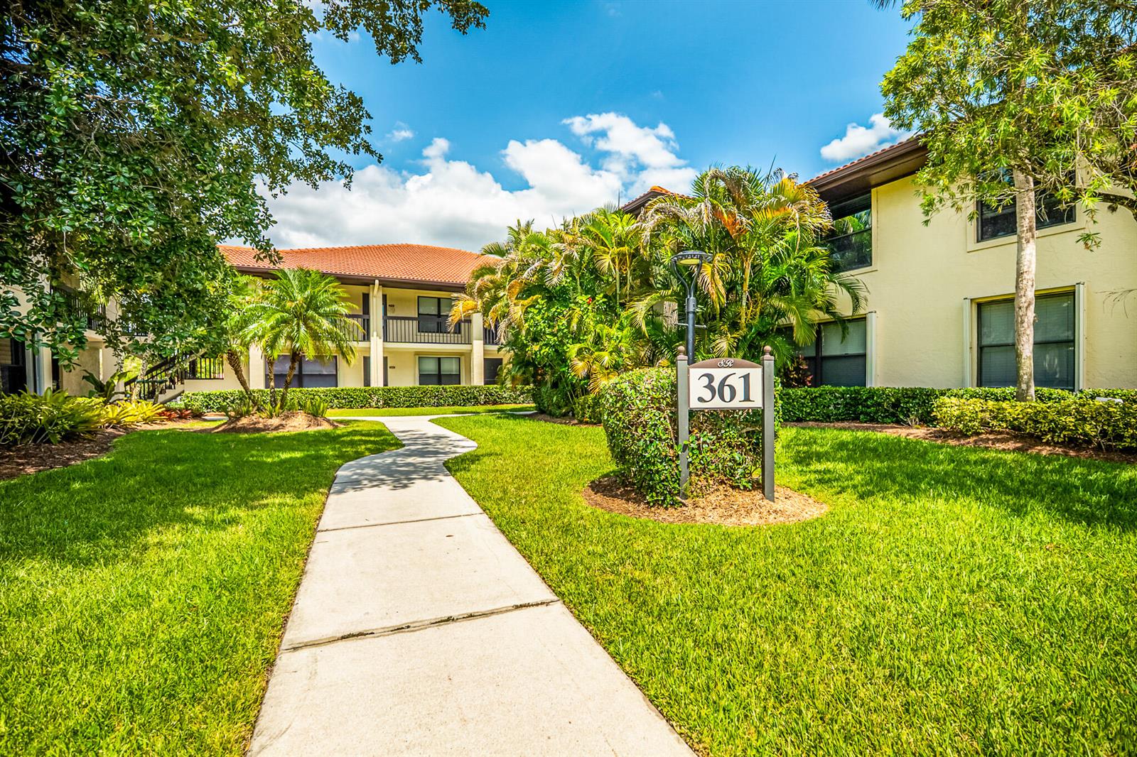 A sidewalk leads toward a two-story apartment building with a red tile roof and landscaping — 361 SW South River Drive # 101, Stuart FL 34997, STUART, FL