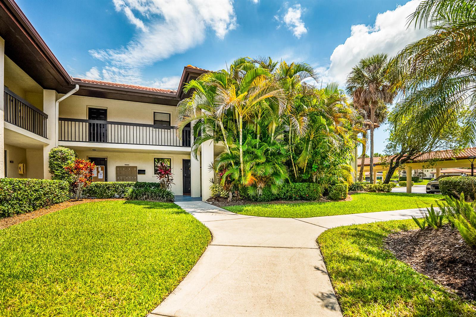 A two-story apartment building exterior with a concrete walkway, lush landscaping, and palm trees — 361 SW South River Drive # 101, Stuart FL 34997, STUART, FL