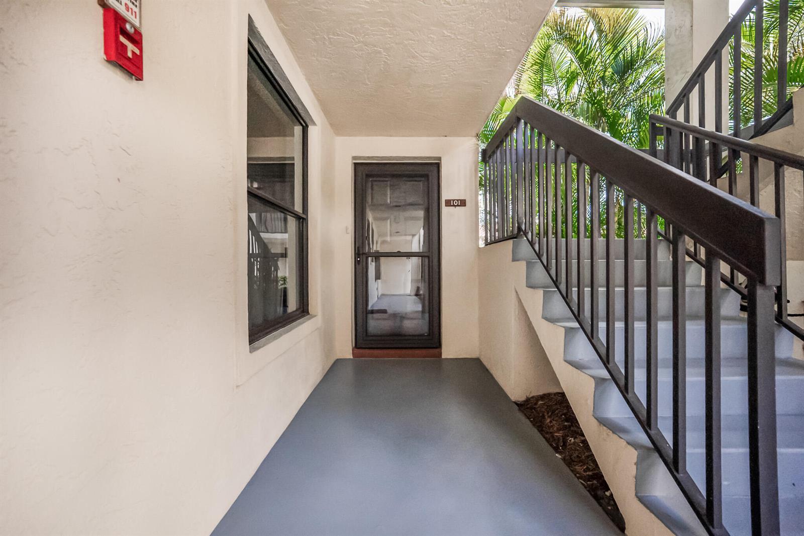 A ground-level apartment entrance features a screen door, a window, and adjacent outdoor stairs — 361 SW South River Drive # 101, Stuart FL 34997, STUART, FL
