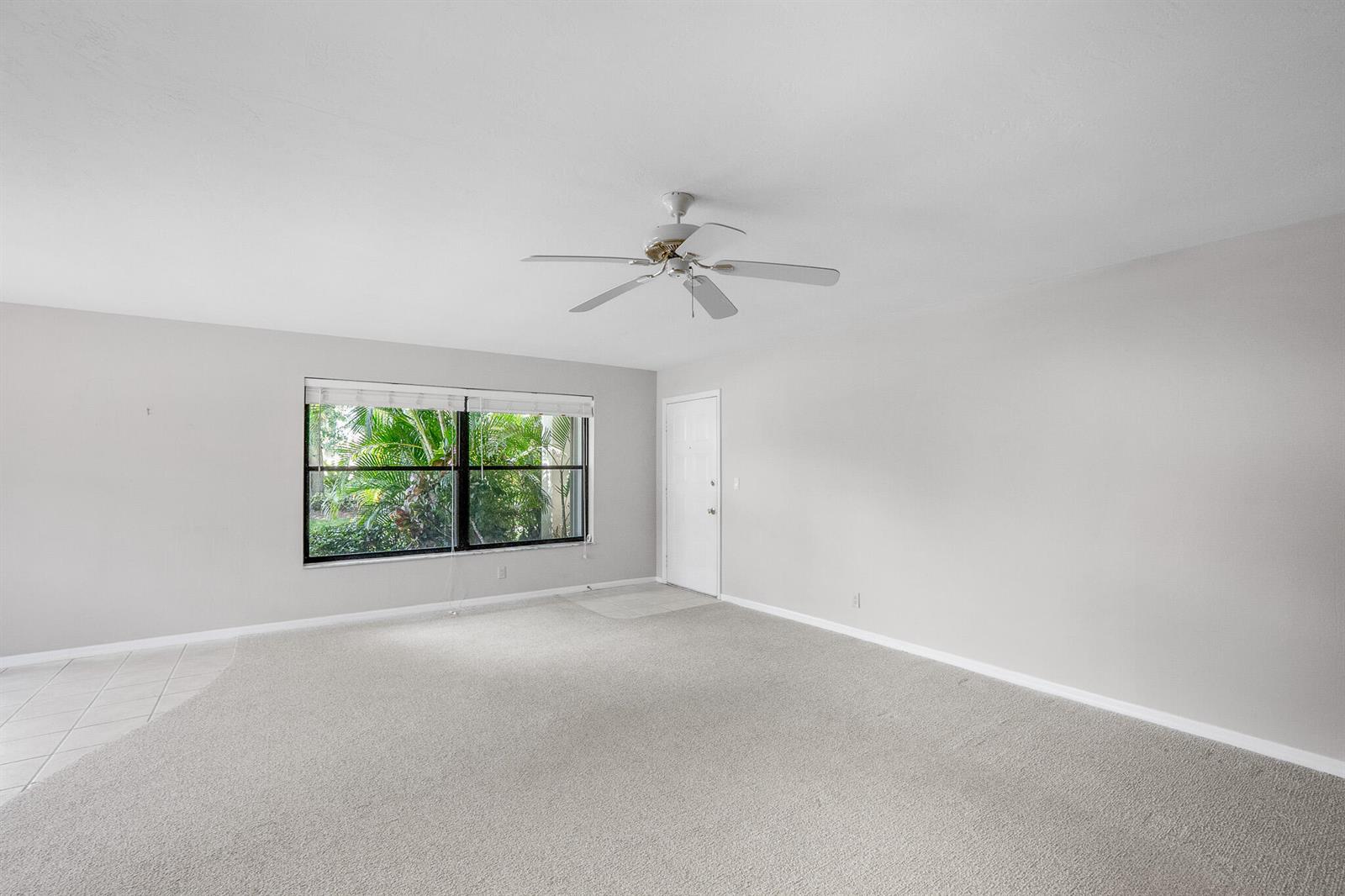 A living room with gray carpet, white walls, a ceiling fan, and a large window — 361 SW South River Drive # 101, Stuart FL 34997, STUART, FL