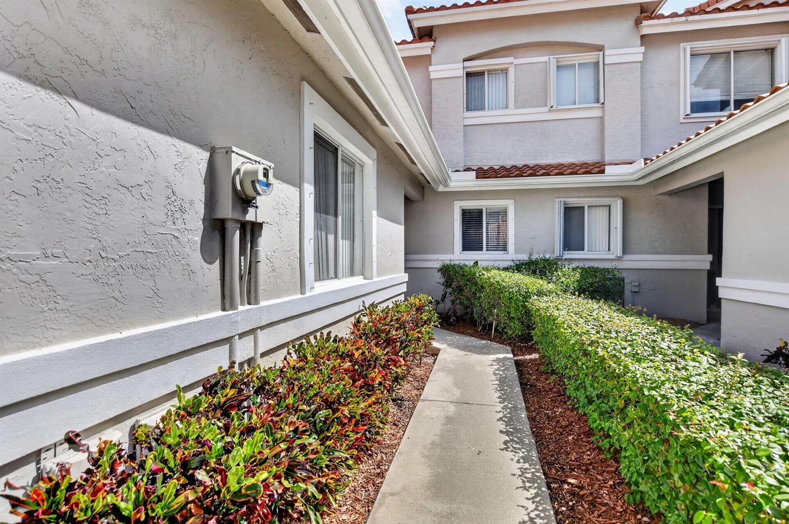 A concrete walkway leads to the entrance of a two-story home with landscaped hedges — 10401 Lake Vista Circle, Boca Raton FL 33498, BOCA RATON, FL