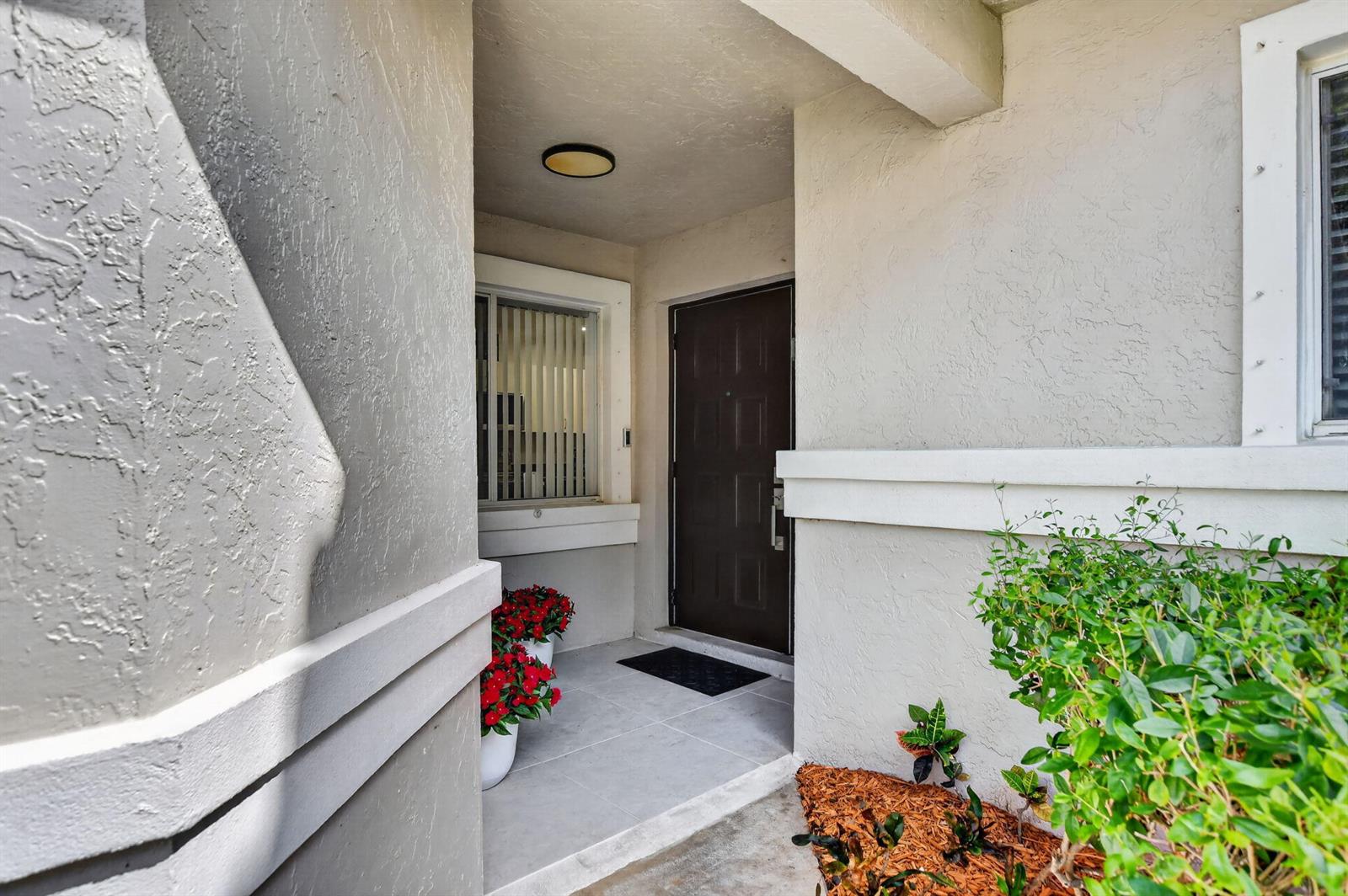 A covered entryway features a dark brown front door, tiled flooring, and potted red flowers — 10401 Lake Vista Circle, Boca Raton FL 33498, BOCA RATON, FL