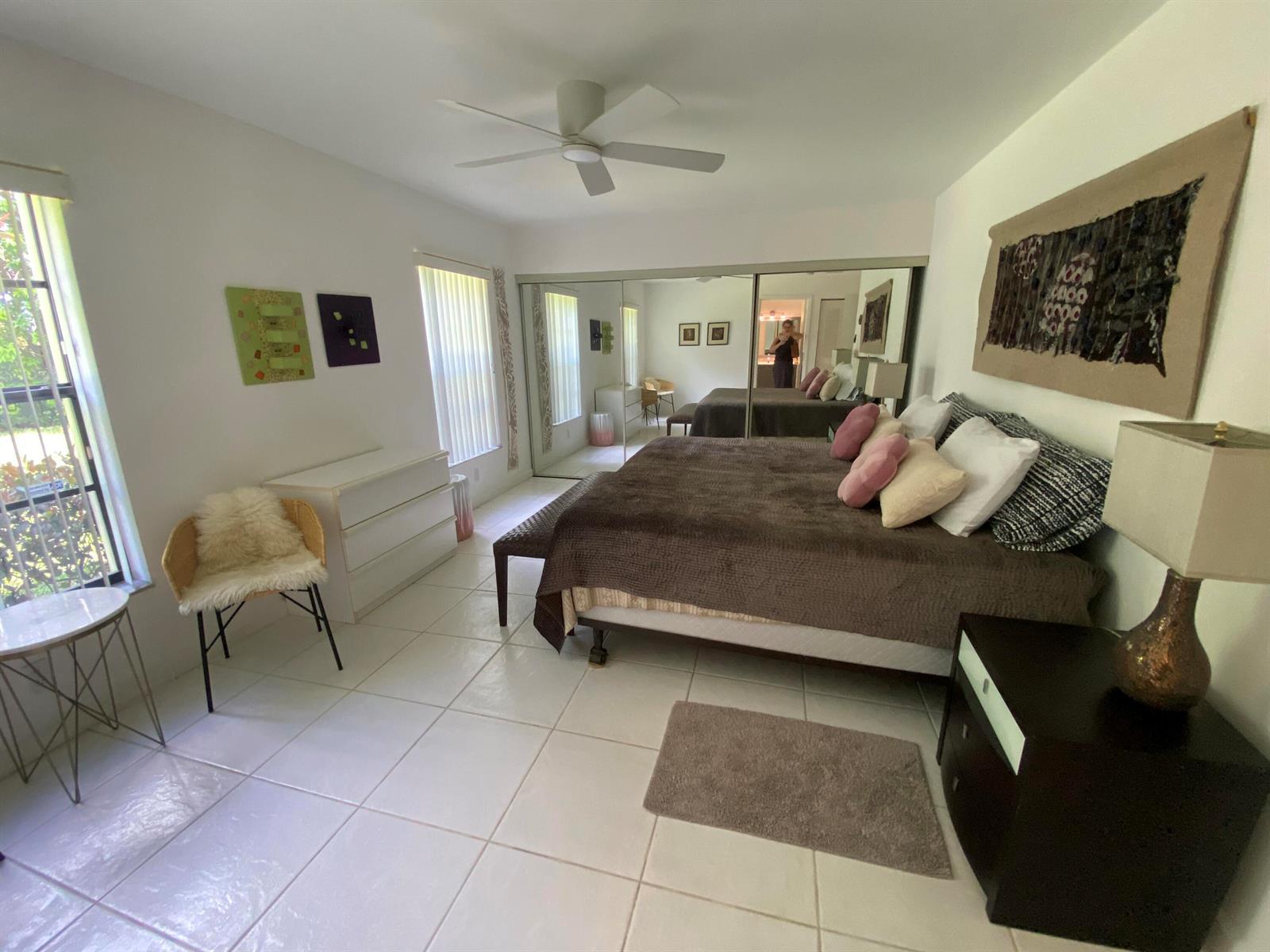 A bedroom with white tile floors, a large bed, mirrored closet doors, and a ceiling fan — 5061 Nesting Way # D, Delray Beach FL 33484, DELRAY BEACH, FL