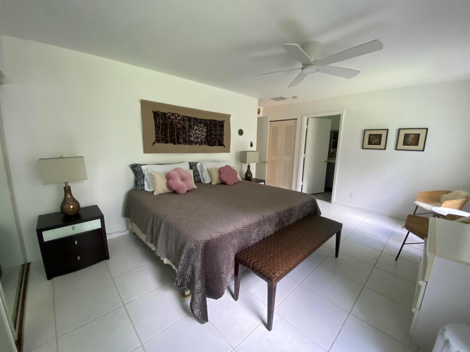 A bedroom features a king bed with a brown coverlet, a bench, and white tile flooring — 5061 Nesting Way # D, Delray Beach FL 33484, DELRAY BEACH, FL