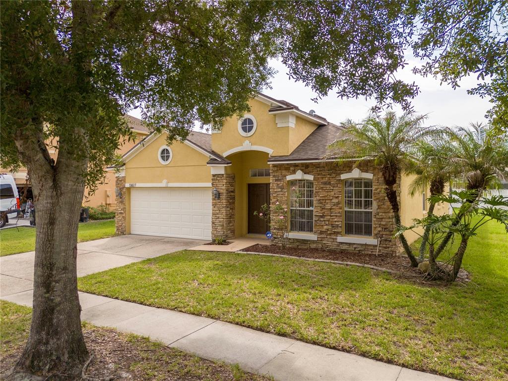 A yellow single-story house with a stone facade, two-car garage, and a front lawn — 13827 HAWKEYE DRIVE, ORLANDO, FL