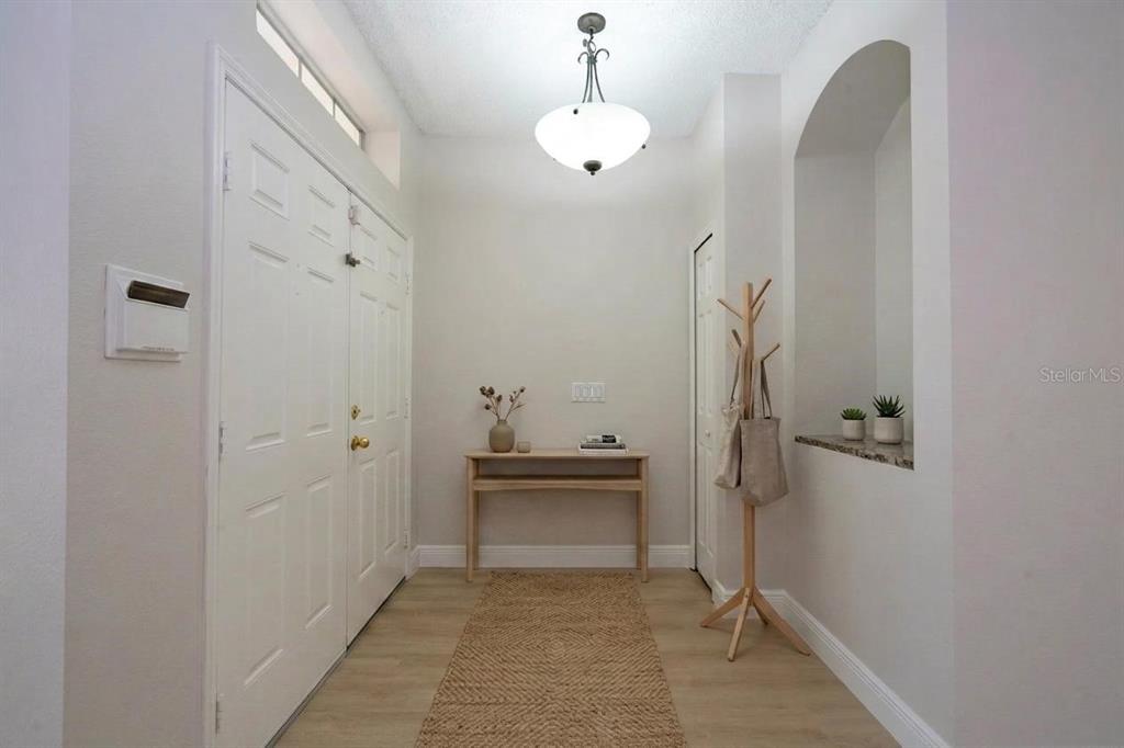 A bright entryway features light wood flooring, a console table, a coat rack, and arched niche — 13827 HAWKEYE DRIVE, ORLANDO, FL