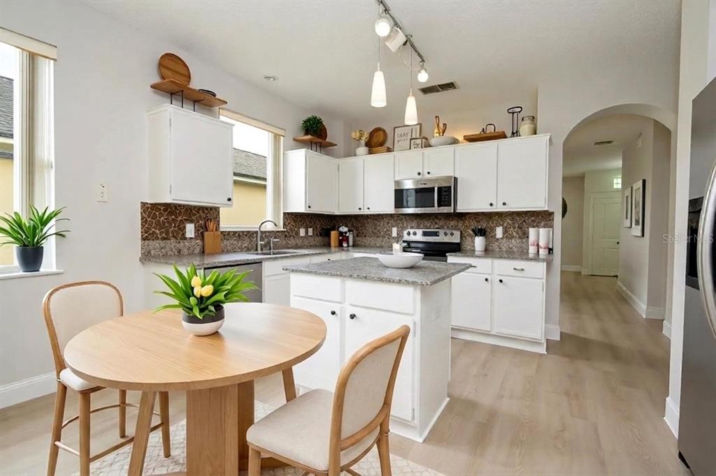 A kitchen features white cabinetry, granite countertops, a central island, and a small dining area — 13827 HAWKEYE DRIVE, ORLANDO, FL
