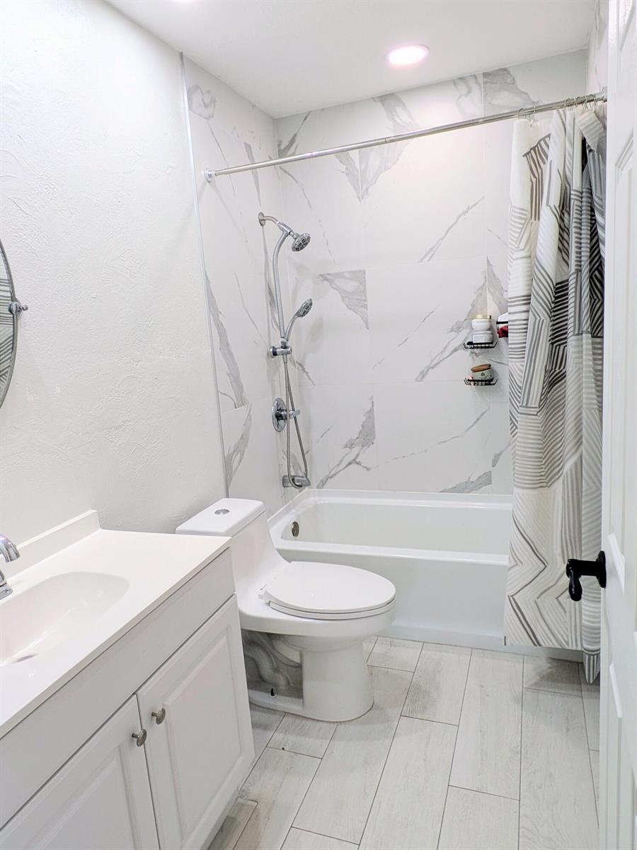 A bathroom features a white vanity, a toilet, and a bathtub with marble-look tile walls — 21089 Brookshire Terrace, Boca Raton FL 33433, BOCA RATON, FL