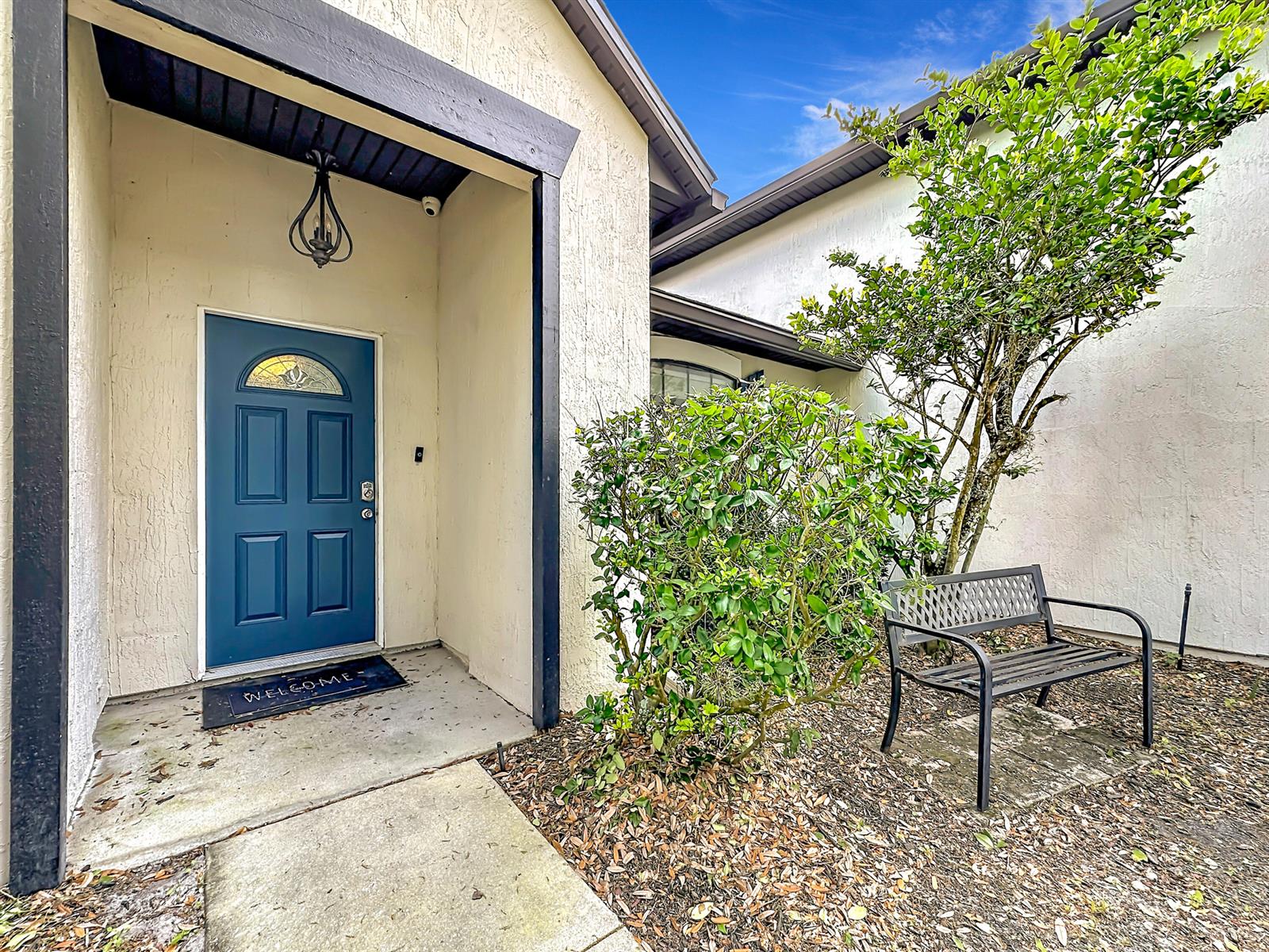 A blue front door with a welcome mat sits beside a bench and a tree — 3371 Classic Oak Court, FL 32065, FL