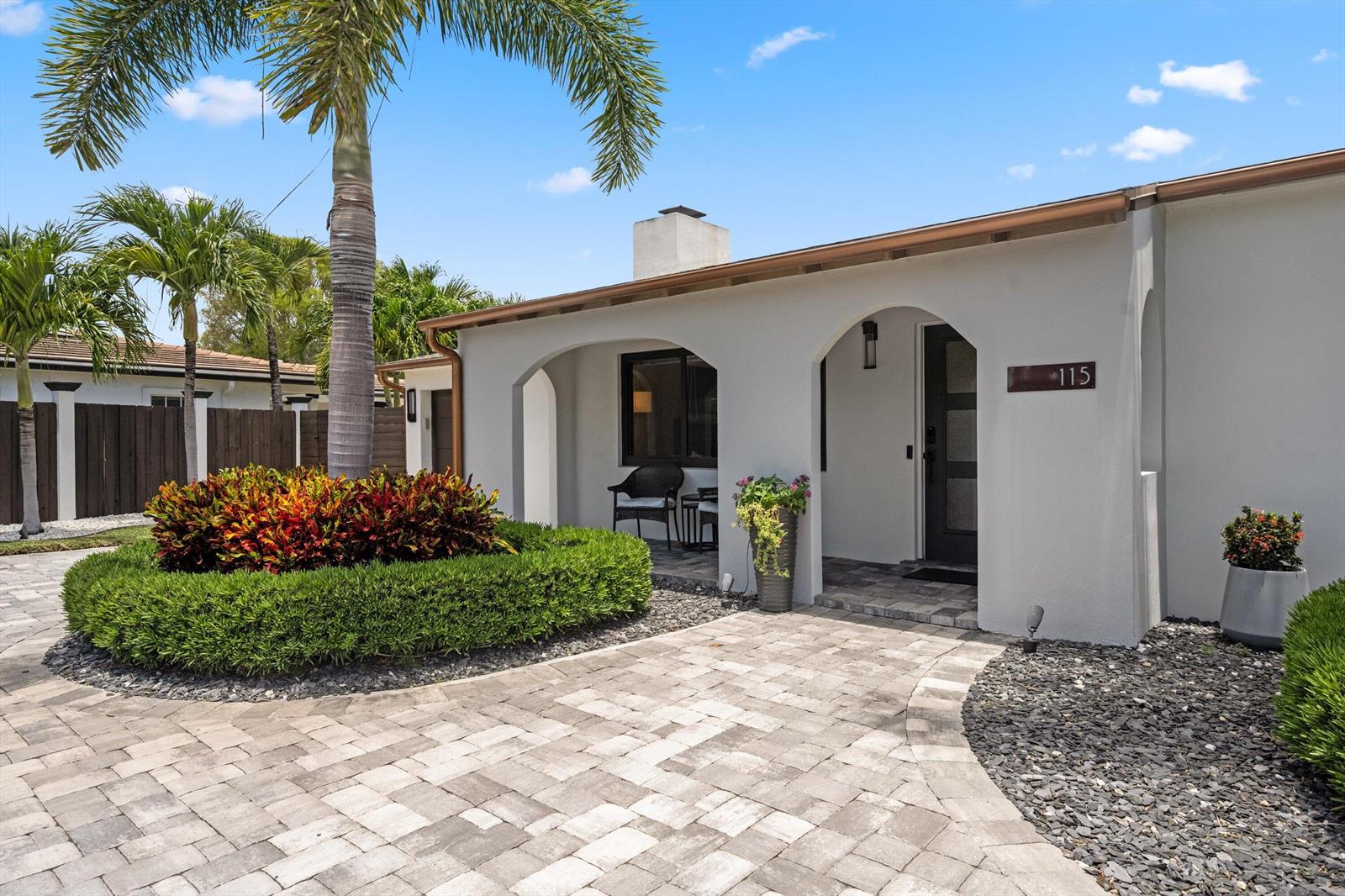A paved walkway leads to the arched entryway of a white house with landscaping — 115 Highland Lane, Delray Beach FL 33444, DELRAY BEACH, FL