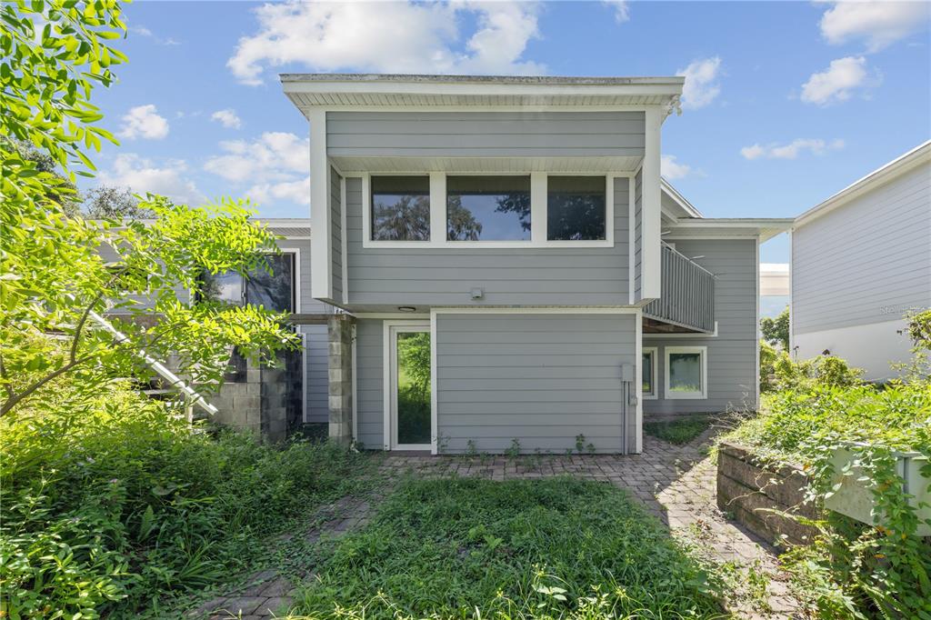 The exterior of a two-story gray house features a paved patio and overgrown landscaping — 932 N HYER AVENUE, ORLANDO, FL