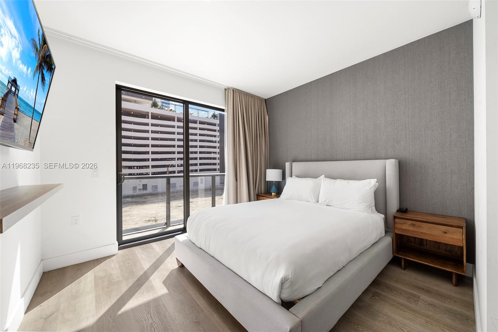 A bedroom features a gray upholstered bed, a textured accent wall, and a balcony view — 229 SW 9th St # 208, Miami FL 33130, MIAMI, FL