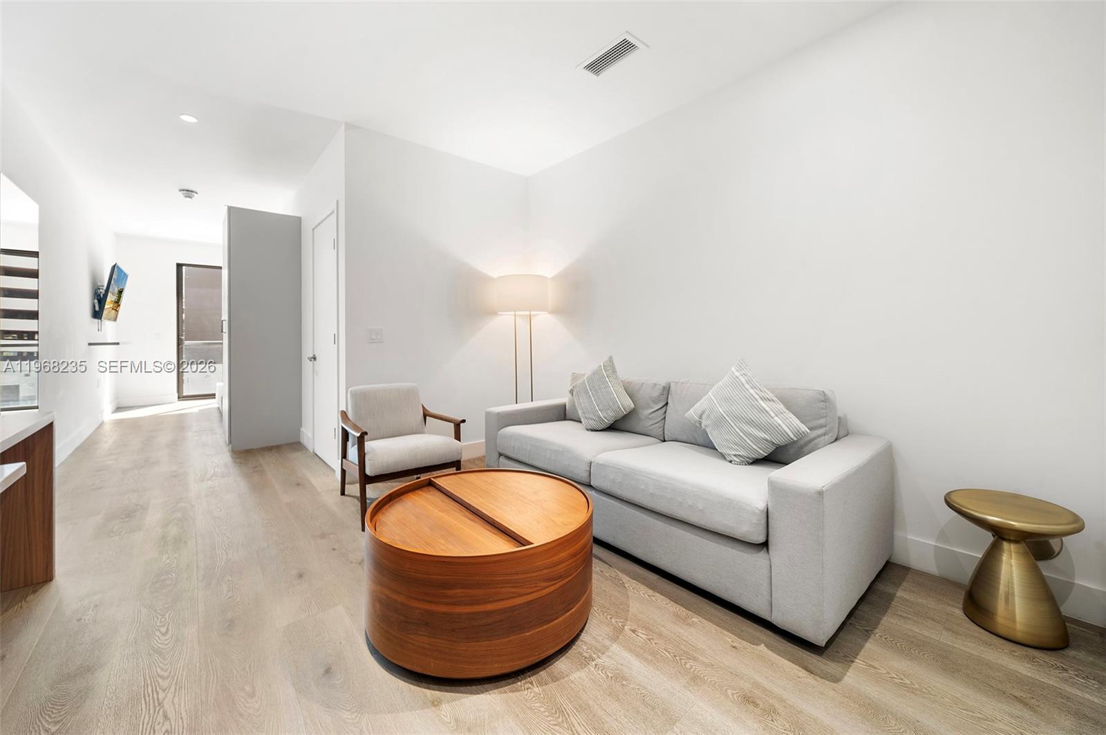 A living room features a gray sofa, a round wooden coffee table, and light wood flooring — 229 SW 9th St # 208, Miami FL 33130, MIAMI, FL