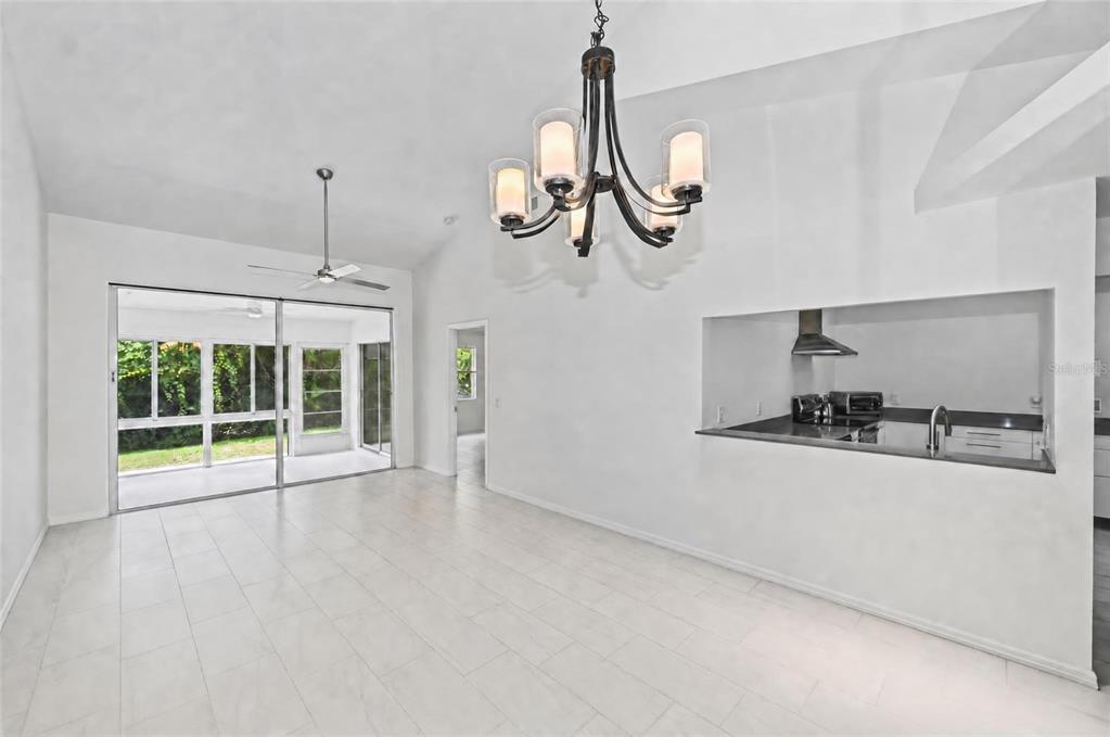 A bright dining area with white tile floors, a chandelier, and a pass-through kitchen window — 5623 MONTE ROSSO ROAD, SARASOTA, FL