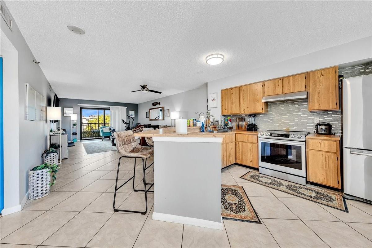 An open-concept kitchen with wood cabinets and a breakfast bar overlooks a living area — 2217 Cypress Island Drive # 507, Pompano Beach FL 33069, POMPANO BEACH, FL