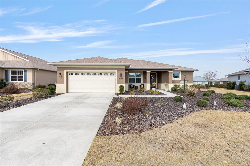 A single-story suburban house with a two-car garage, tan stucco exterior, and dark mulch landscaping — 10525 SW 90TH STREET ROAD, OCALA, FL