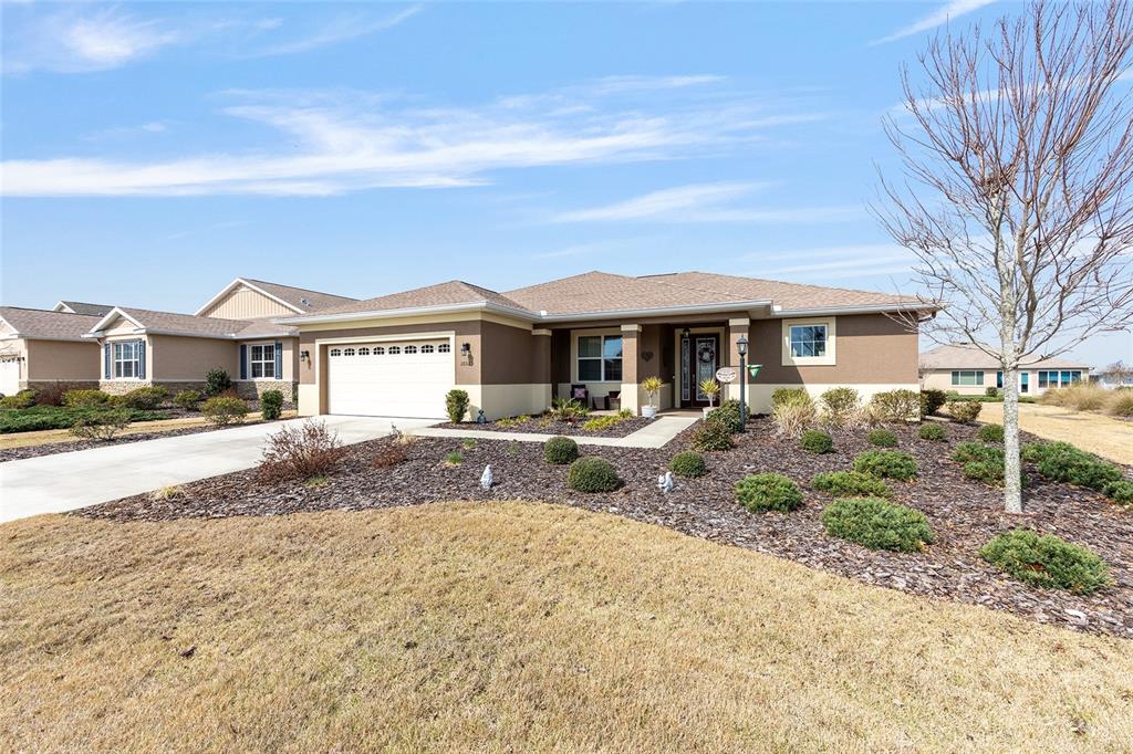 A single-story house with a tan stucco exterior, a two-car garage, and landscaped front yard — 10525 SW 90TH STREET ROAD, OCALA, FL