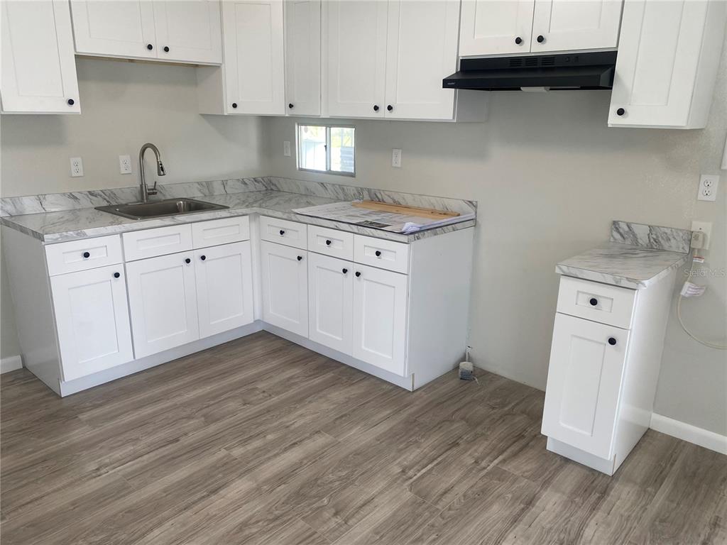 A kitchen features white cabinets, marble-patterned countertops, and light wood-look flooring — 6841 OSPREY LANE, HUDSON, FL