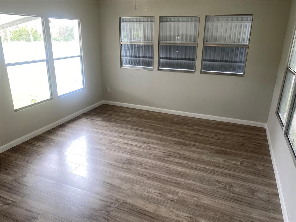 An empty room features light-colored walls, wood-look flooring, and several windows with metal awnings — 6841 OSPREY LANE, HUDSON, FL