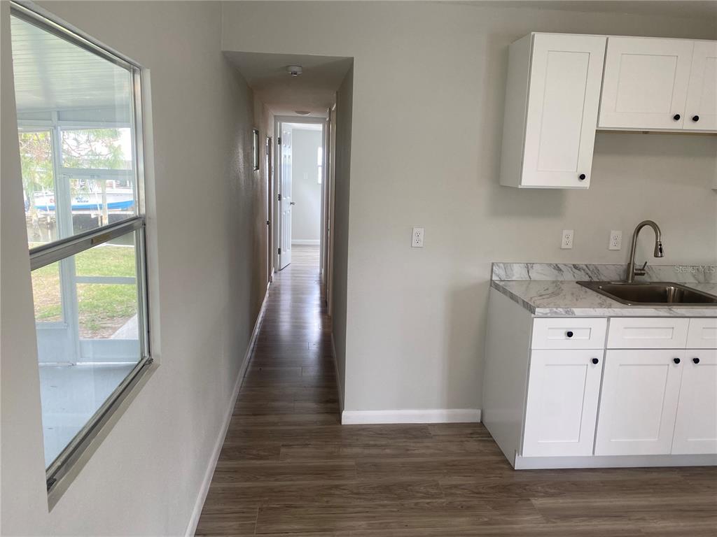 A kitchen with white cabinets and marble-look countertops leads into a hallway with wood flooring — 6841 OSPREY LANE, HUDSON, FL