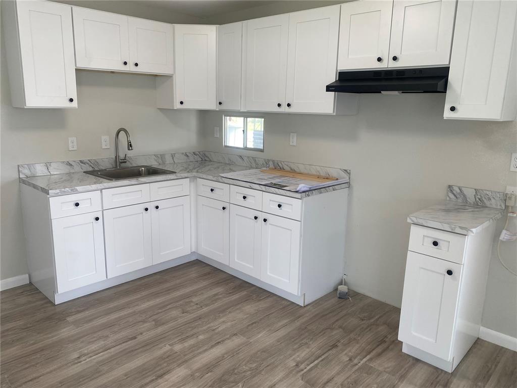 A kitchen features white shaker cabinets, marble-patterned laminate countertops, and light wood-look flooring — 6841 OSPREY LANE, HUDSON, FL