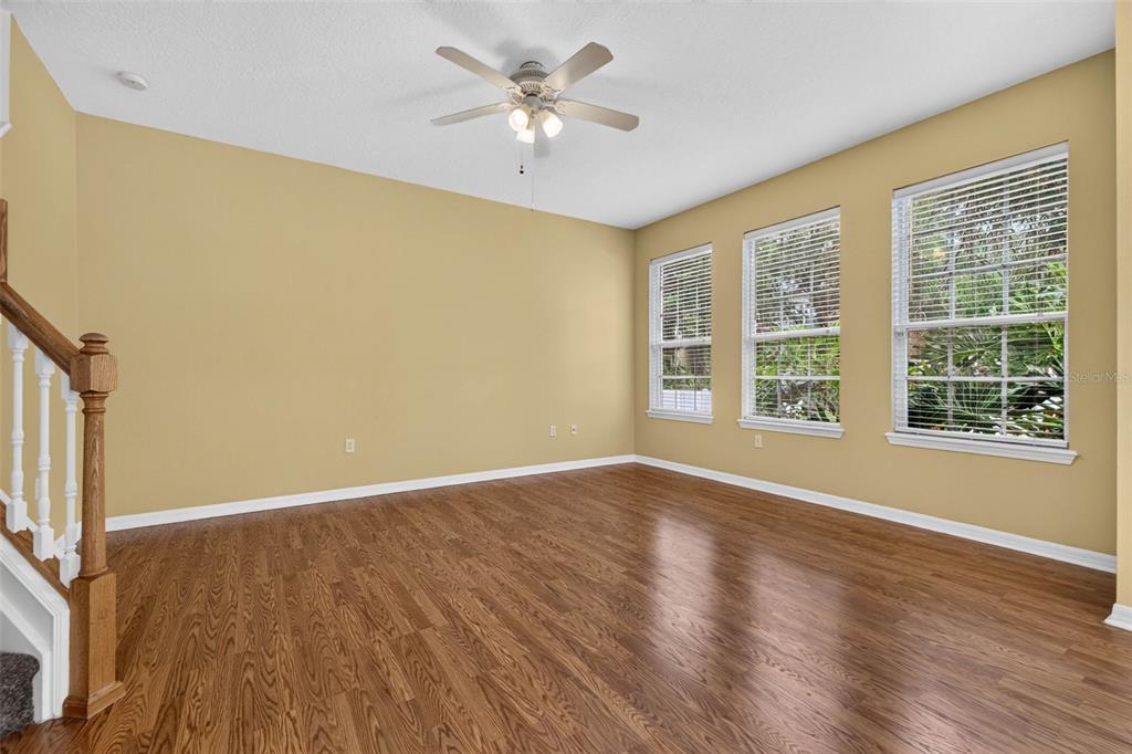 An empty room with yellow walls, wood-look flooring, a ceiling fan, and three windows — 27747 PLEASURE RIDE LOOP, WESLEY CHAPEL, FL
