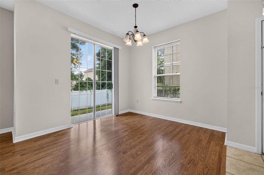 An empty dining area features wood-look flooring, a chandelier, a sliding glass door, and a window — 27747 PLEASURE RIDE LOOP, WESLEY CHAPEL, FL
