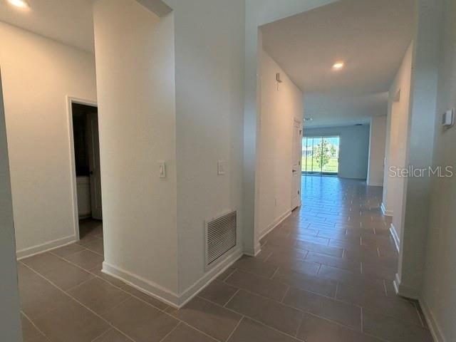 A hallway with light-colored tile flooring leads toward a bright room with sliding glass doors — 2959 CAMDEN WAY, DAVENPORT, FL