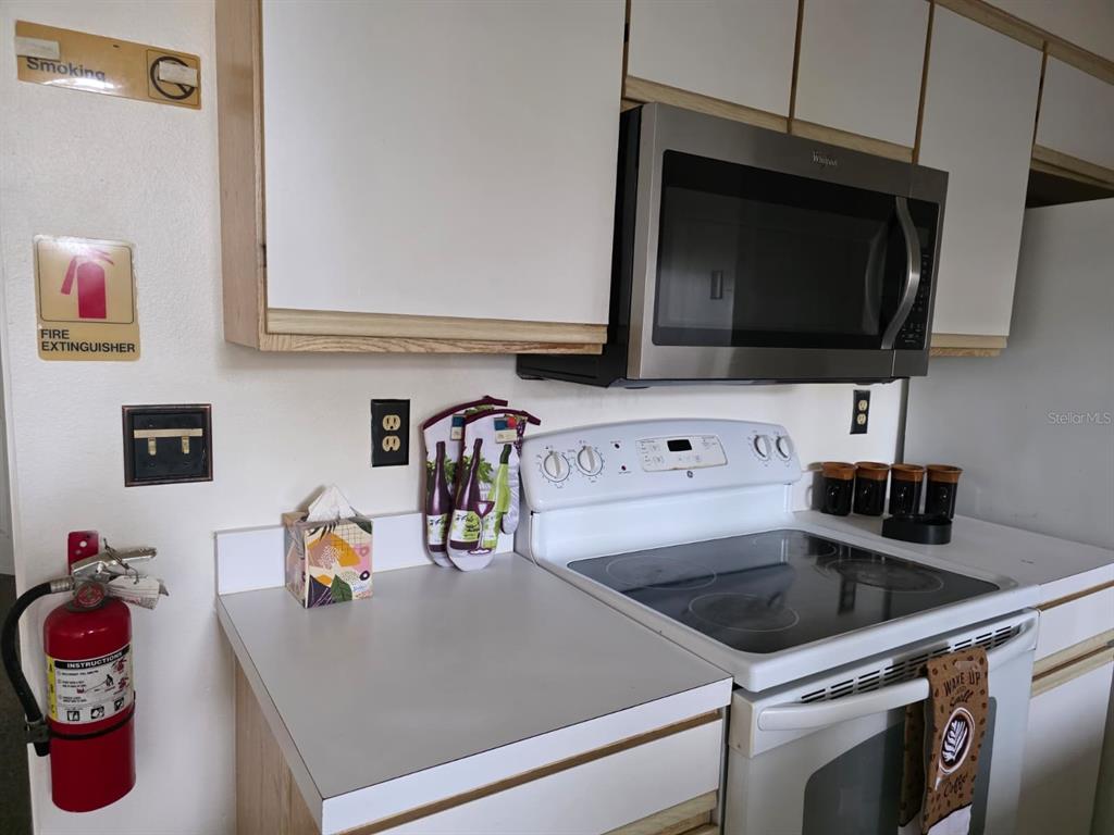 A kitchen features white cabinets, a stainless steel microwave, a white stove, and a fire extinguisher — 2456 SWEETWATER CLUB CIRCLE UNIT 20, KISSIMMEE, FL