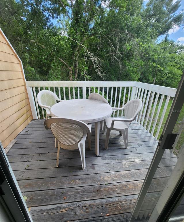 A wooden deck features a white plastic table and four chairs overlooking a wooded area — 2456 SWEETWATER CLUB CIRCLE UNIT 20, KISSIMMEE, FL