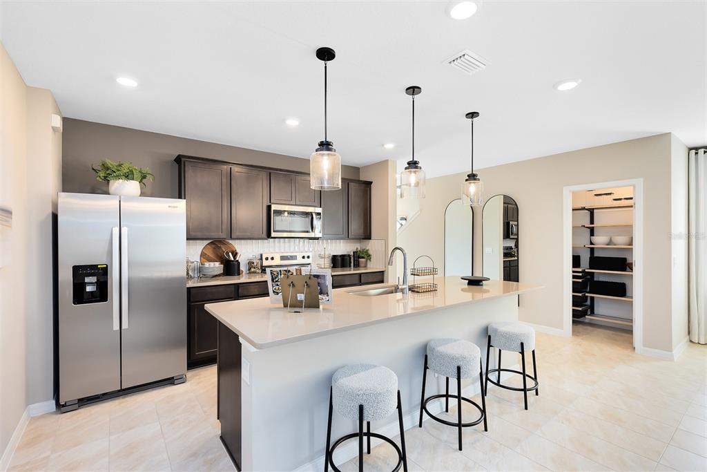 A modern kitchen features dark wood cabinets, a large quartz island, and stainless steel appliances — 6838 CREEK FALLS ALLEY, CLERMONT, FL