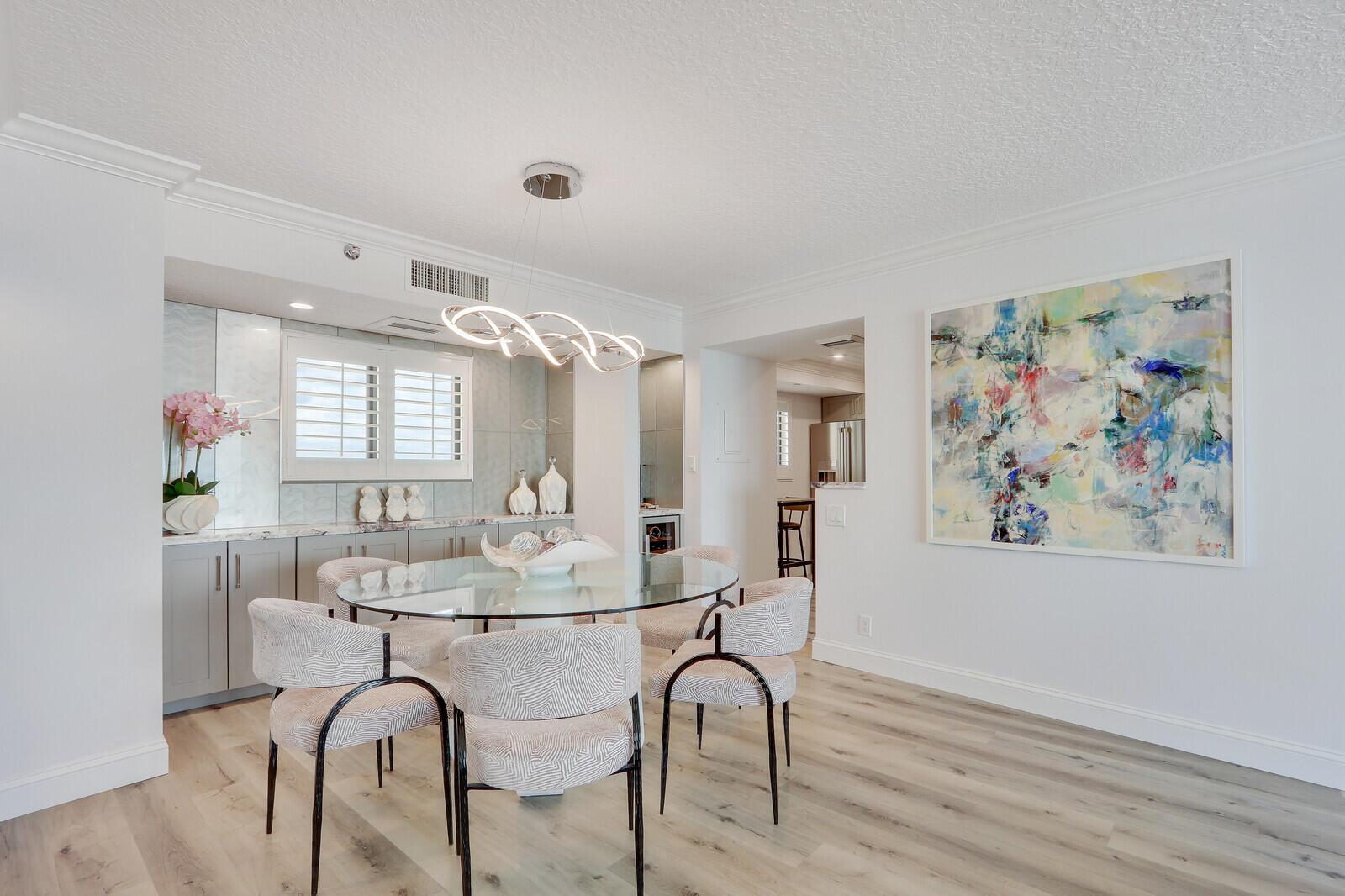 A dining room features a glass table, patterned chairs, a modern chandelier, and abstract art — 100 Ocean Trail Way, Jupiter FL 33477, JUPITER, FL