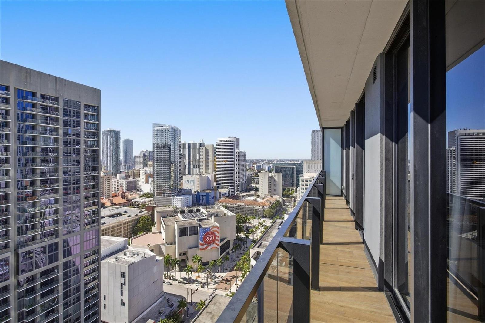 A high-rise balcony with wood-look flooring overlooks a dense urban cityscape under a clear sky — 398 NE 5th Street # 2017, Miami FL 33132, MIAMI, FL